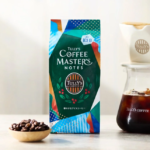 Bag of Tullys Coffee Masters Notes iced coffee mix beside a glass carafe of cold brew with a small bowl of coffee beans in front