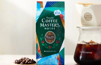 Bag of Tully's Coffee Masters Notes iced coffee mix beside a glass carafe of cold brew, with a small bowl of coffee beans in front.