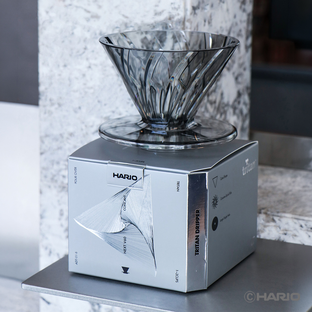 Clear glass cone shaped pour over coffee dripper sits atop a white HARIO product box labeled Tritan Dripper