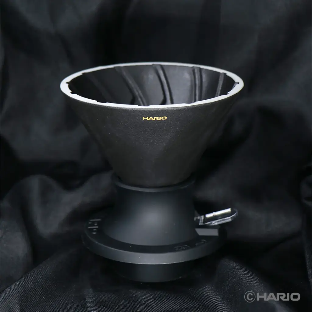 Black Hario pour over coffee dripper with ridged interior on a wide base placed on black fabric