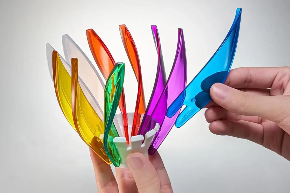 Several translucent colored plastic blades are fanned out around a white central hub with a hand holding a blue blade ready to attach