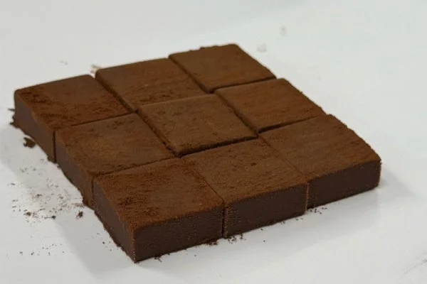 ココアパウダーがまぶされた四角い生チョコレートが、白い表面にきれいに並べられています。