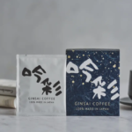 Two Gin sai Coffee packages on a marble counter white and dark blue boxes with a cup nearby