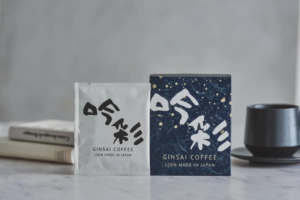 Two Gin sai Coffee packages on a marble counter white and dark blue boxes with a cup nearby