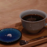 White ceramic cup of black coffee on a wooden tray with a small blue dish containing sugar and a spoon