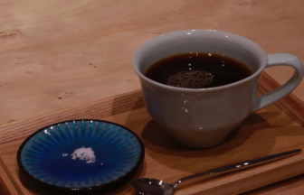 White ceramic cup of black coffee on a wooden tray with a small blue dish containing sugar and a spoon