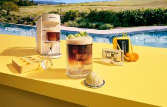 Poolside yellow counter with a white espresso machine, a tall glass of iced coffee, and an ice tray on a sunny day by a pool (text reads 'Yuzu Vanilla Over Ice').