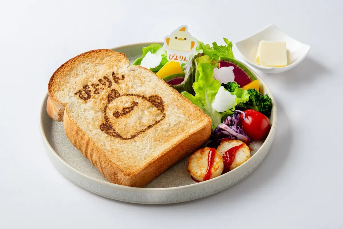「ぴよりん」というキャラクターが描かれたトーストがメインのワンプレート朝食です。色とりどりの新鮮なサラダ、ミニハッシュポテト、そして別添えのバターが添えられており、可愛らしくてバランスの取れた食事が表現されています。