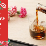 Mothers Day gift card with floral design beside a glass of iced cola on a wooden table
