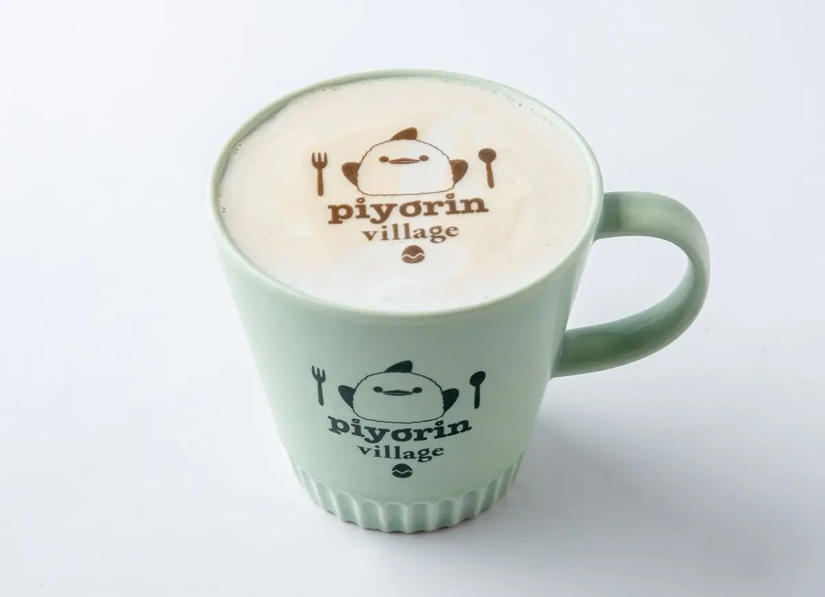 「piyorin village」のロゴとキャラクターが描かれた薄緑色のマグカップに、同じキャラクターのラテアートが施されたカフェラテが入っています。