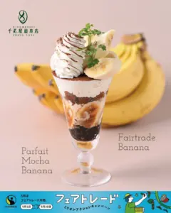 Banana parfait in a tall glass topped with whipped cream and banana slices with Fairtrade branding in the top left and a blue promotional banner at the bottom