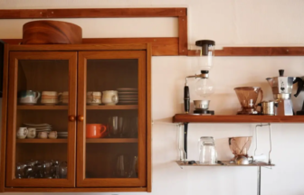 Wooden cabinet with glass doors containing dishes coffee gear on a shelf to the right