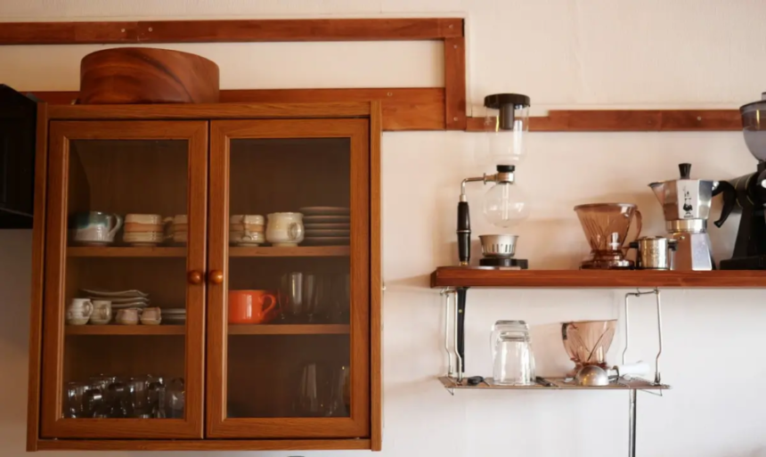 Wooden cabinet with glass doors containing dishes coffee gear on a shelf to the right