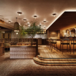Warm upscale bar lounge with a long wooden bar tall stools and tropical plants under soft ambient lighting