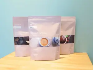 Three Ultora Soy Diet Protein pouches on a wooden table against a teal wall displayed in a row with soft lighting