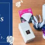 Left a dark blue card reading Happy Fathers Day with white floral corners and Japanese text right a wooden table displaying Fathers Day gifts including white gift boxes a blue Fathers Day card and a colorful stand with rainbow colored pieces arranged as a gift set