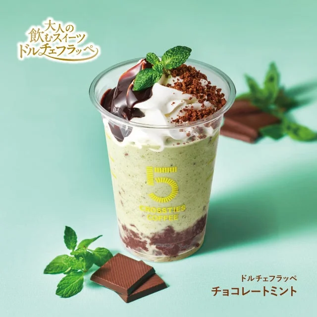 Green matcha drink in a clear cup topped with whipped cream chocolate drizzle and a mint leaf with chocolate pieces nearby