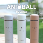 Three pastel AniBall by Zooie bottles with cute cat faces on a wooden table outdoors The brand name appears above