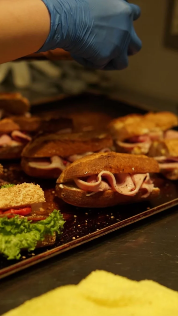 Gloved hand arranging ham and cheese sliders on a baking sheet in a kitchen