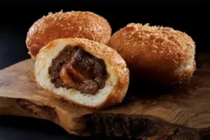Three fried dough balls on a wooden board one cut open to reveal a rich chocolate filling