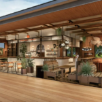 Open plan cafe with wood accents a curved bar counter hanging lights and potted plants large windows in the background