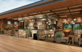 Open-plan cafe with wood accents, a curved bar counter, hanging lights, and potted plants; large windows in the background.