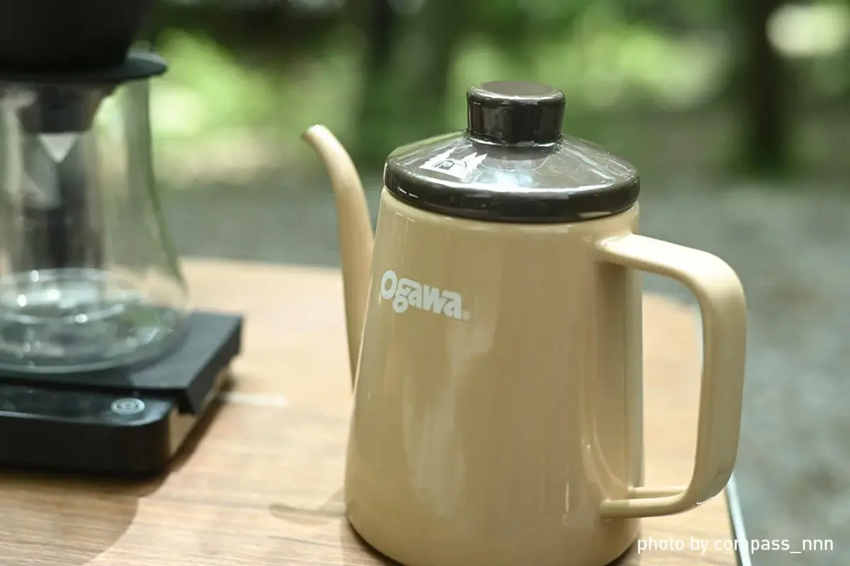 Beige kettle with black lid and handle on a wooden table outdoors brand logo visible