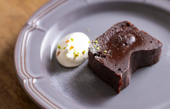 Slice of dark chocolate cake with a scoop of vanilla ice cream on a gray plate sprinkled with pistachio bits on top of the ice cream