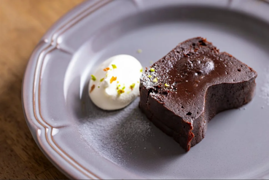 Slice of dark chocolate cake with a scoop of vanilla ice cream on a gray plate sprinkled with pistachio bits on top of the ice cream