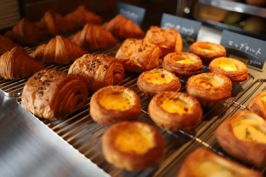 Assorted pastries on a bakery display rack including croissants and cream filled Danish pastries sultry with flaky layers