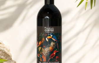 Bottle of Paikaji Coffee Black Coffee with a vibrant tropical label on a light stone surface outdoors