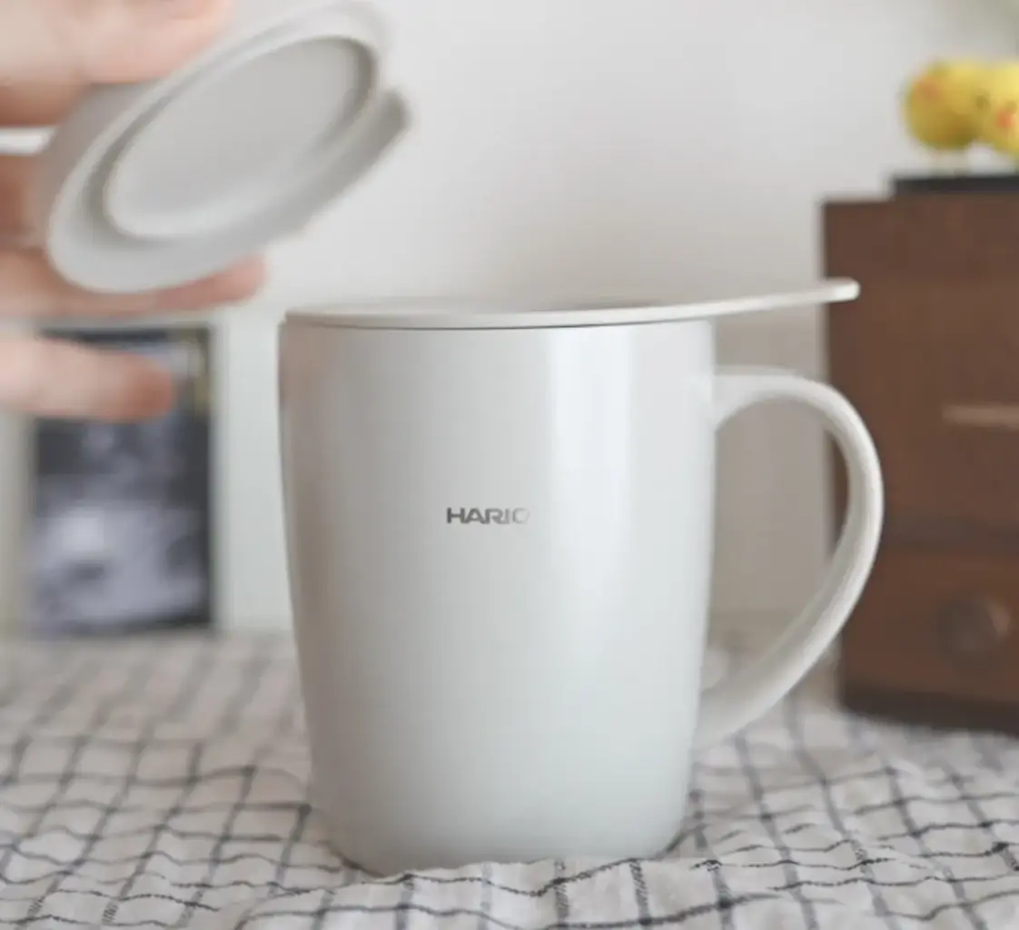 1780402074OtRFVTr69L3IpDClc2ueb4PY | コーヒーステーション Hand lifting the lid off a white ceramic HARIO mug on a checkered tablecloth