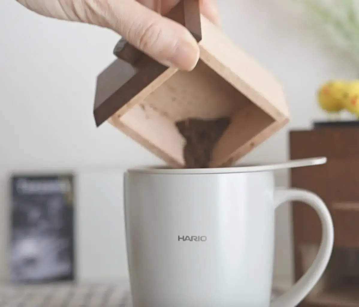 1780402594cvl1wYQh4IeHs9yVk7dimUAn | コーヒーステーション Close up of a hand pouring ground coffee from a wooden funnel into a white Hario mug