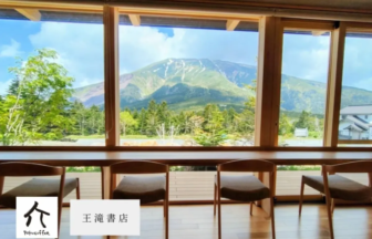 Cafe interior with a wooden counter and row of chairs large windows overlooking trees and a mountain range outside