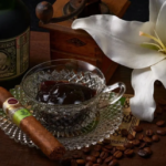Crystal glass with dark liquor and a cigar resting on a crystal saucer beside a bottle of Diplomatico rum and a white lily