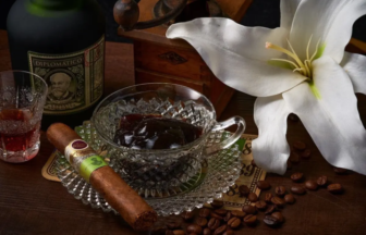 Crystal glass with dark liquor and a cigar resting on a crystal saucer beside a bottle of Diplomatico rum and a white lily