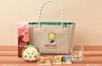 Beige tote bag with a Coji Coji logo on a wooden surface surrounded by snacks a plush lion toy a honey peach juice carton and a glass