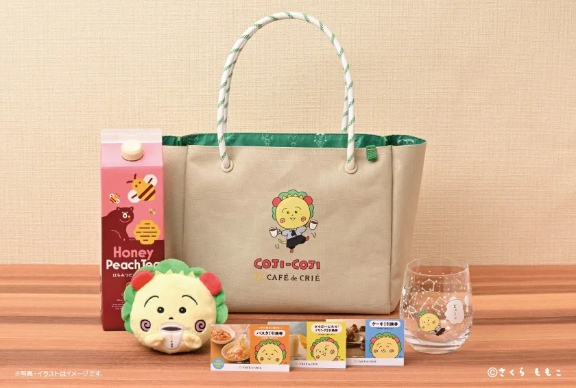 Beige tote bag with a Coji Coji logo on a wooden surface surrounded by snacks a plush lion toy a honey peach juice carton and a glass