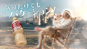 Humorous ad scene a man relaxing in a deck chair with a giant bottle of tea floating beside him Japanese text overhead and a factory skyline in the background