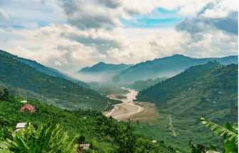 Winding river through a lush green valley flanked by misty mountains under a cloudy blue sky