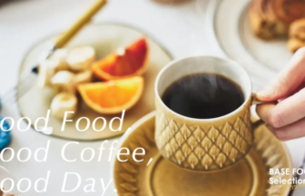 Cup of black coffee in a patterned mug on a saucer with a plate of citrus fruit and pastries in the background