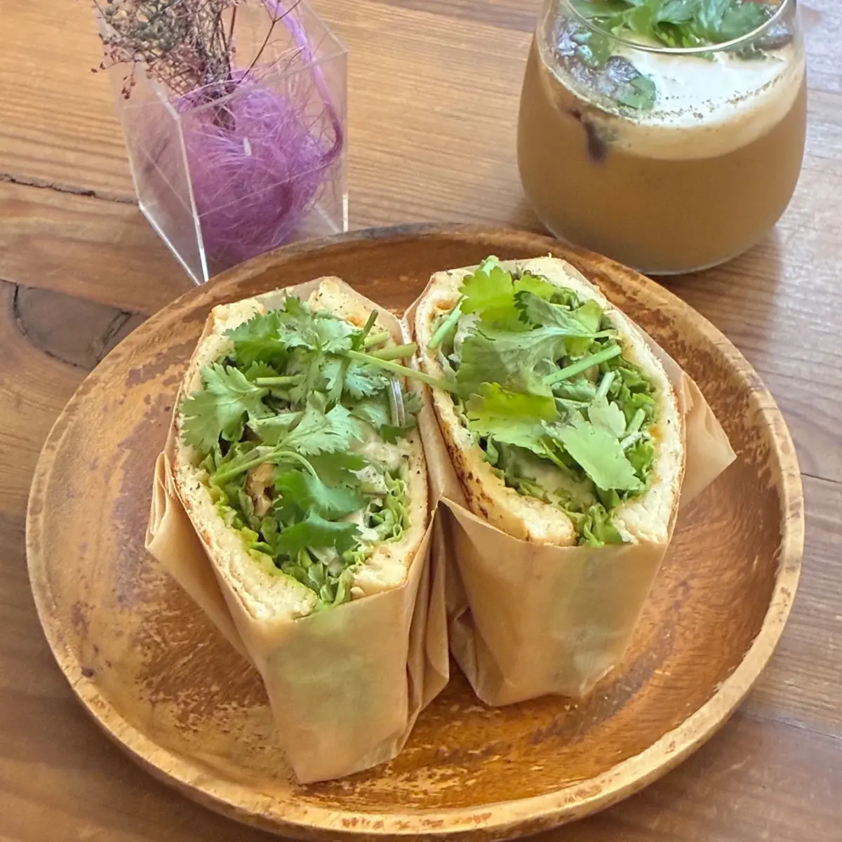 木製のプレートに盛られた、コリアンダーやレタスがたっぷりのヘルシーなサンドイッチと、飲み物