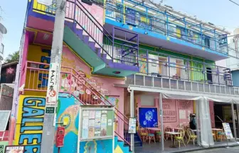 Colorful three story building with graffiti pink stairs and outdoor cafe seating on a sunny street edge