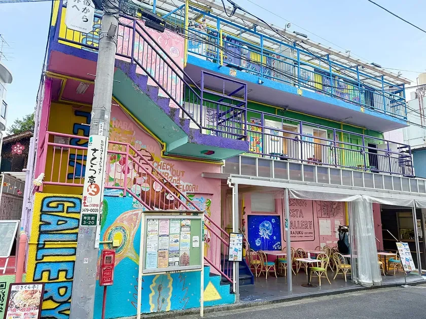 Colorful three story building with graffiti pink stairs and outdoor cafe seating on a sunny street edge