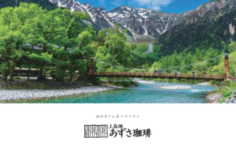 Suspension bridge over a turquoise river in a lush mountain valley with snowy peaks in the distance.