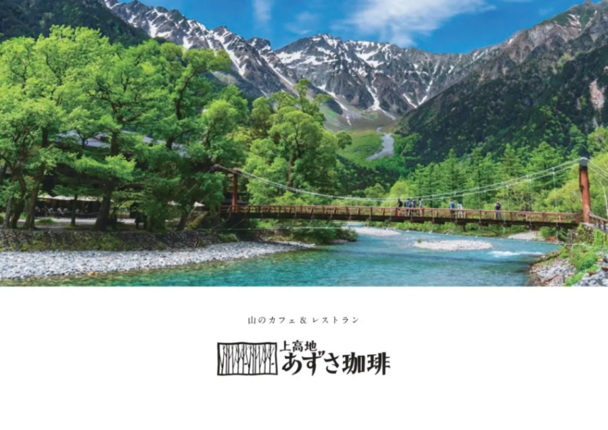 Suspension bridge over a turquoise river in a lush mountain valley with snowy peaks in the distance