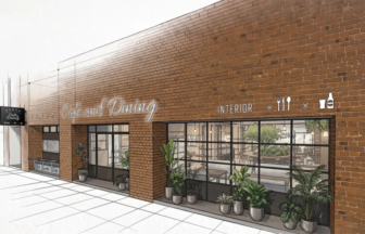Exterior of a brick-c walkway cafe with a large glass storefront; interior dining space visible through windows, potted plants outside.