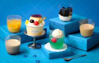 Assorted desserts on a bright blue display a small topped cake green jelly with a cherry and several creamy drinks in cups on blue platforms