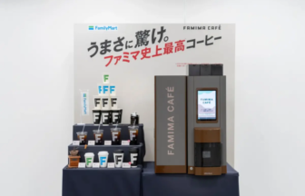 Promotional display with a brown and black Famima Café coffee machine and stacked cups on a dark table branding visible on the poster behind it