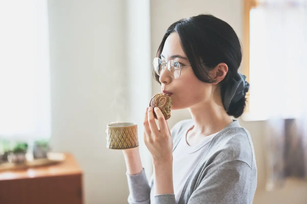 女性がコーヒーとパンを手にしている様子